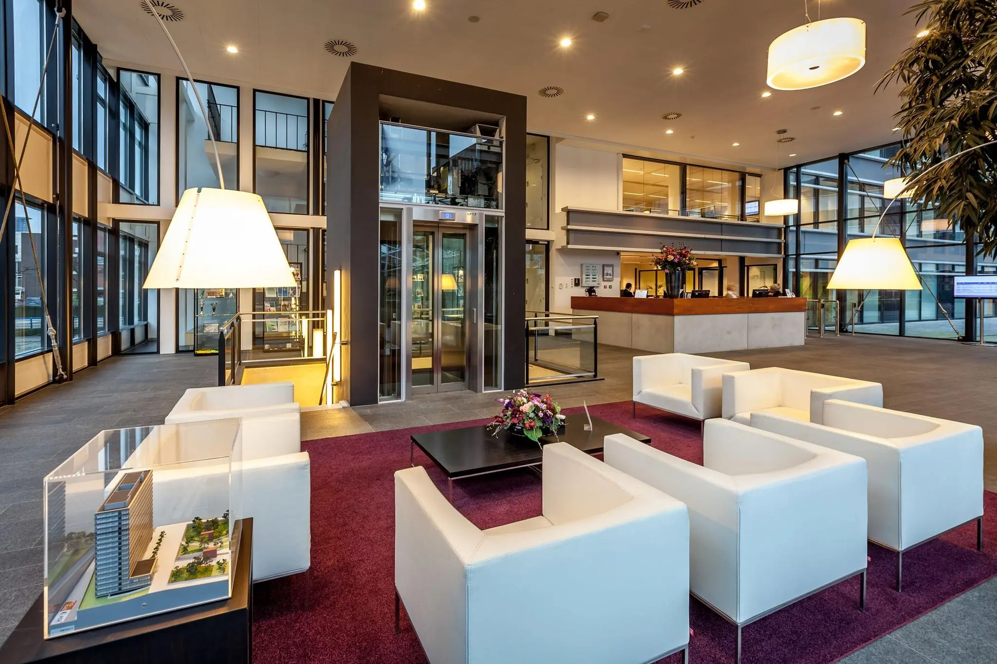 Moderne ontvangsthal aan de Prinses Beatrixlaan met witte zithoeken, een lift, balie en maquette van een gebouw.